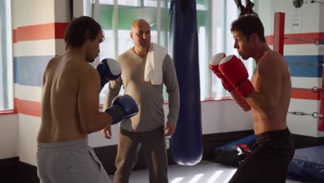 two caucasian men boxing with a coach in boxing ring