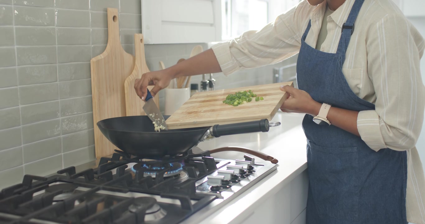 Đầu bếp đang gạt rau xanh thái nhỏ và tỏi vào chảo nóng trên bếp ga để bắt đầu nấu ăn