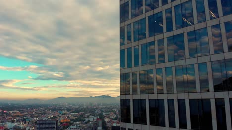 drone ascendiendo al lado del reflejo del cielo nublado de la mañana en las ventanas de edificios altos paisaje urbano