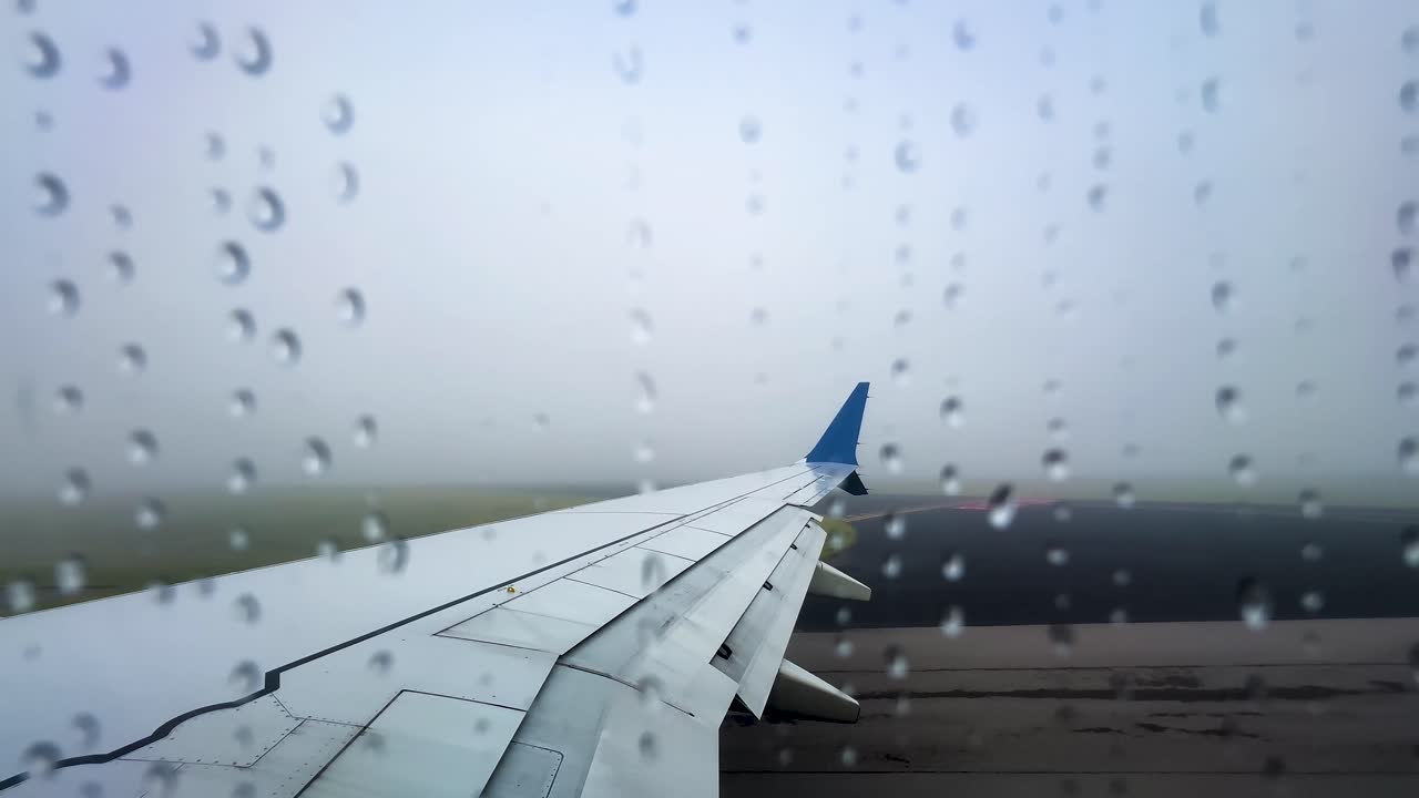 Close-up view of water droplets clinging to an airplane window as the aircraft begins its takeoff roll
