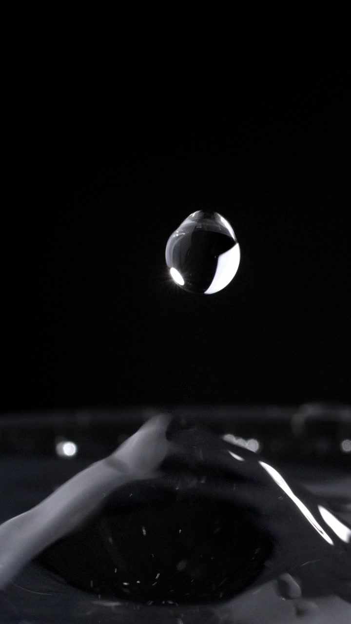 Vertical Shot Of Water Droplets Splashing On Water Surface In Glass With Black Background, Close-Up