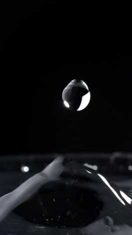 vertical shot of water droplets splashing on water surface in glass with black background, close-up