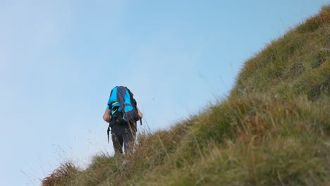 rear view hiker with backpack walks on hiking trail through grassy slopes