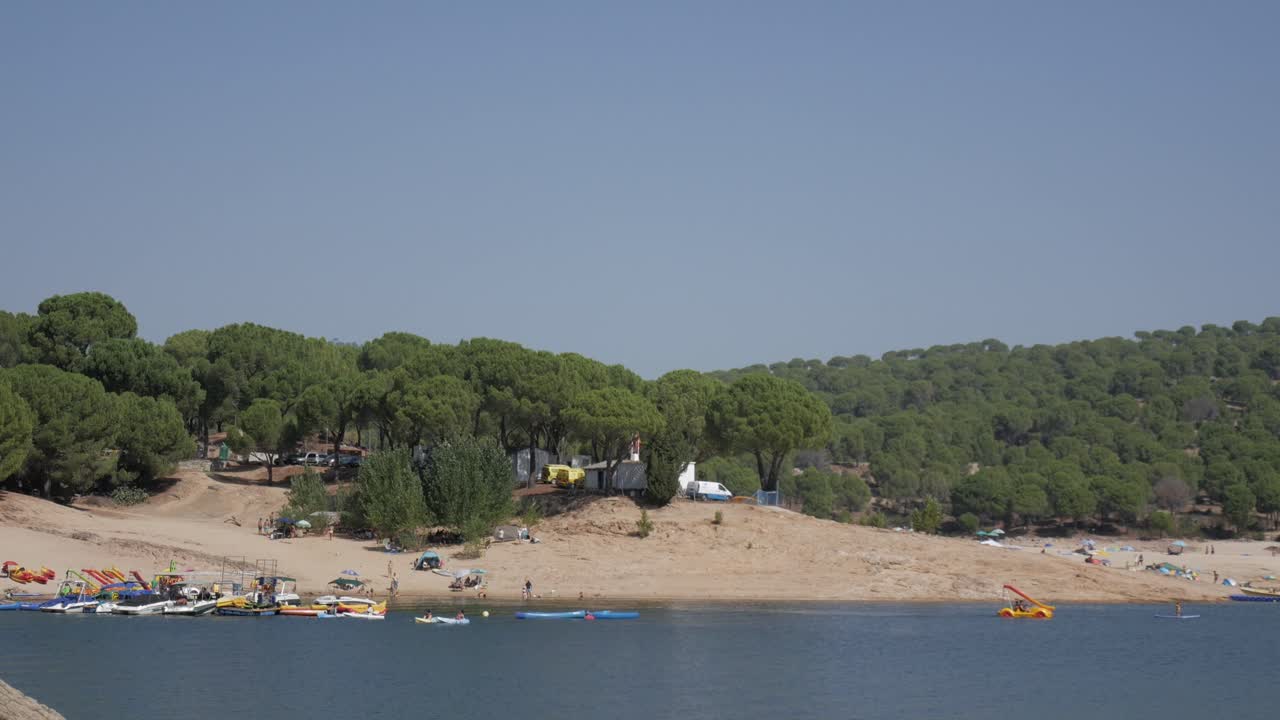 Tranquil beach scene at Embalse de San Juan in Madrid, with boats and trees
