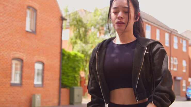 Giovane donna che si allena su una strada urbana con auricolari wireless, controllando lo smartwatch prima di correre
