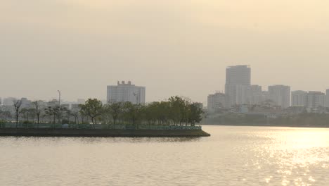 Lake-water-ripples-and-glistens-in-Sunlight-as-vehicles-of-Hanoi-travel-on