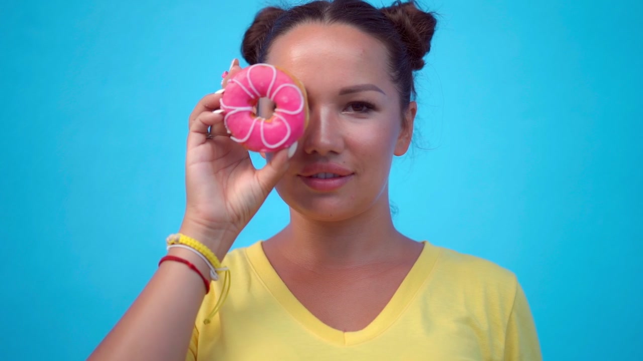 Giovane donna che tiene una ciambella rosa sull'occhio