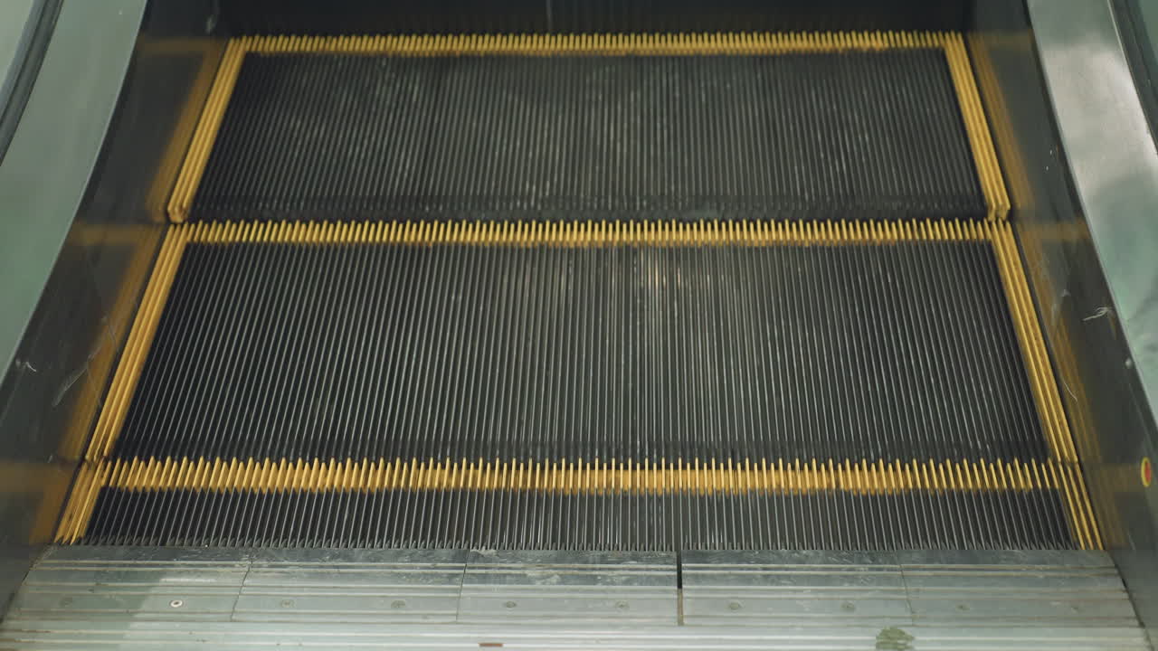 Close up of moving escalator steps with distinct yellow comb edges and black grooved surface in indoor shopping mall environment, showcasing motion, detail, and modern public infrastructure design