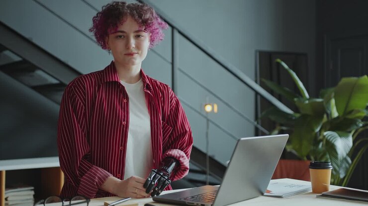 Portræt af smilende pige med protesearm sidder ved skrivebord på kontor