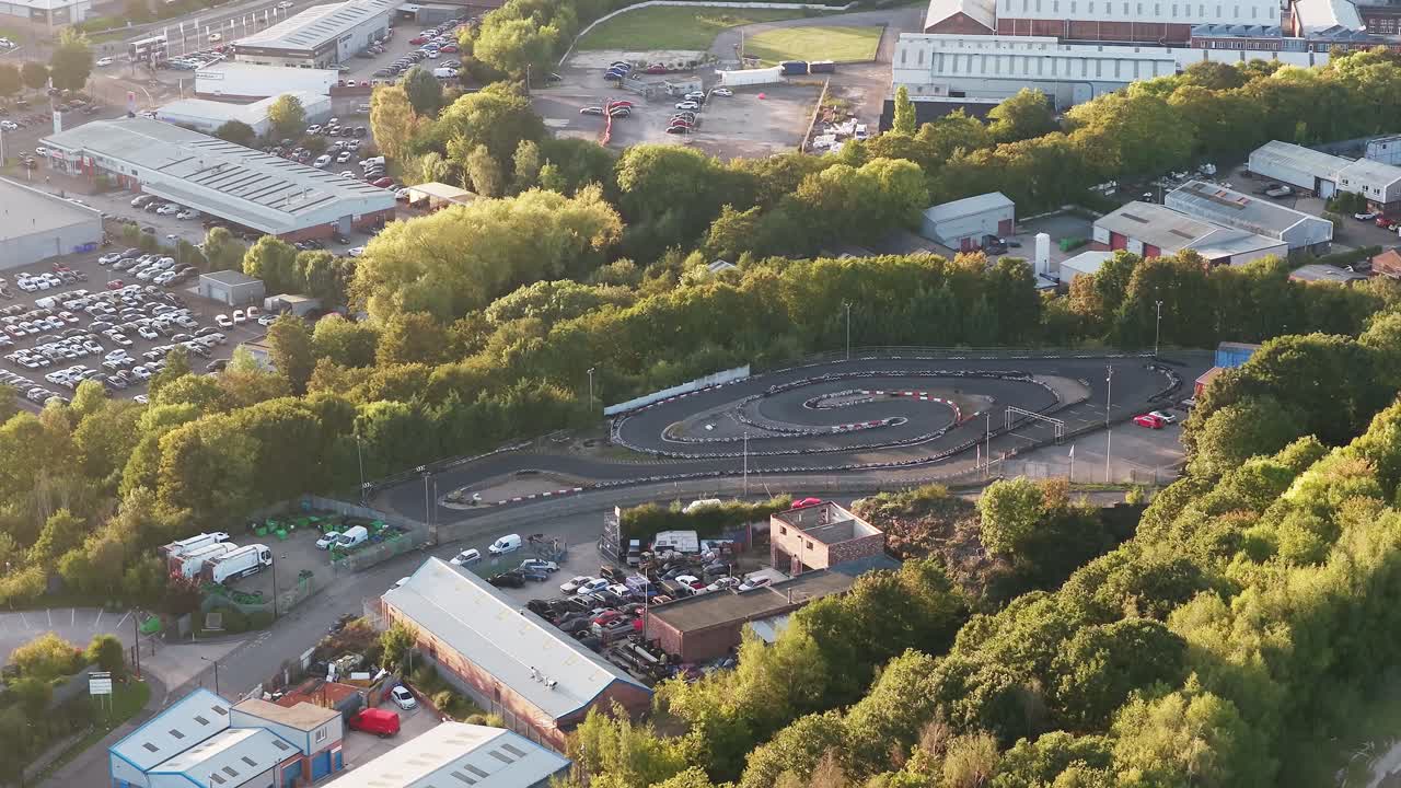 Drone captures a winding go-kart track in Sheffield, active with racers and bordered by warehouses, parking lots, and dense green trees—showcasing urban recreation in an industrial setting