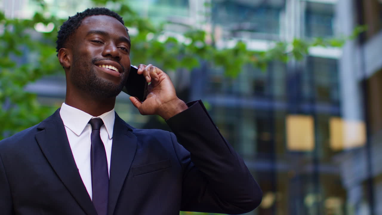 Smiling Young Businessman Wearing Suit Talking On Mobile Phone Standing Outside Offices In The Financial District Of The City Of London UK