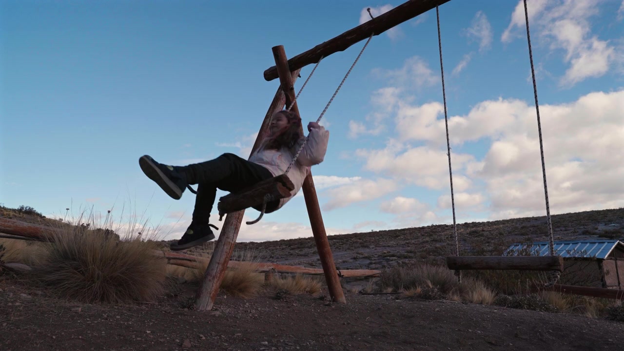 Young woman enjoying a countryside swing during sunset light in a remote mountain destination.