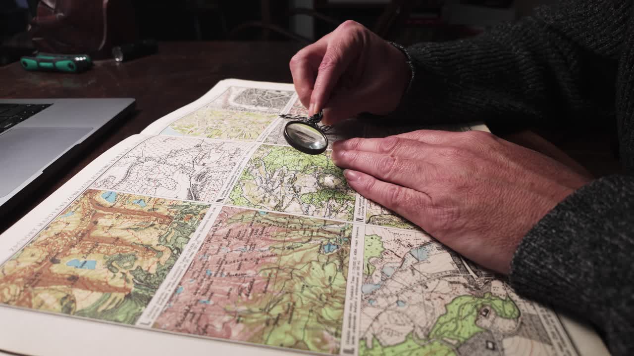 Researcher studies old geographical atlas map archive with magnifier