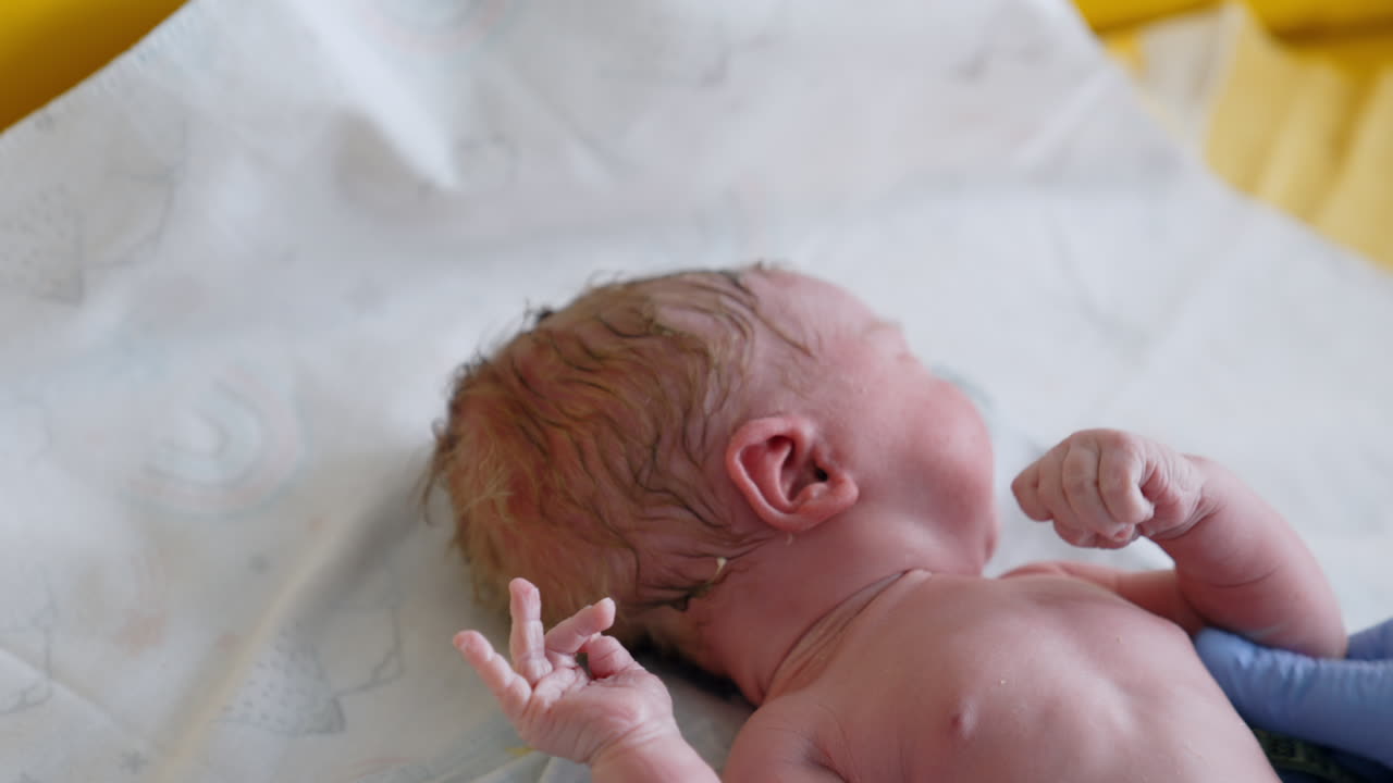 Adorable naked newborn lies on the table. Gloved hands of a medic use measuring tape to know the kid's parameters at birth. Close up.