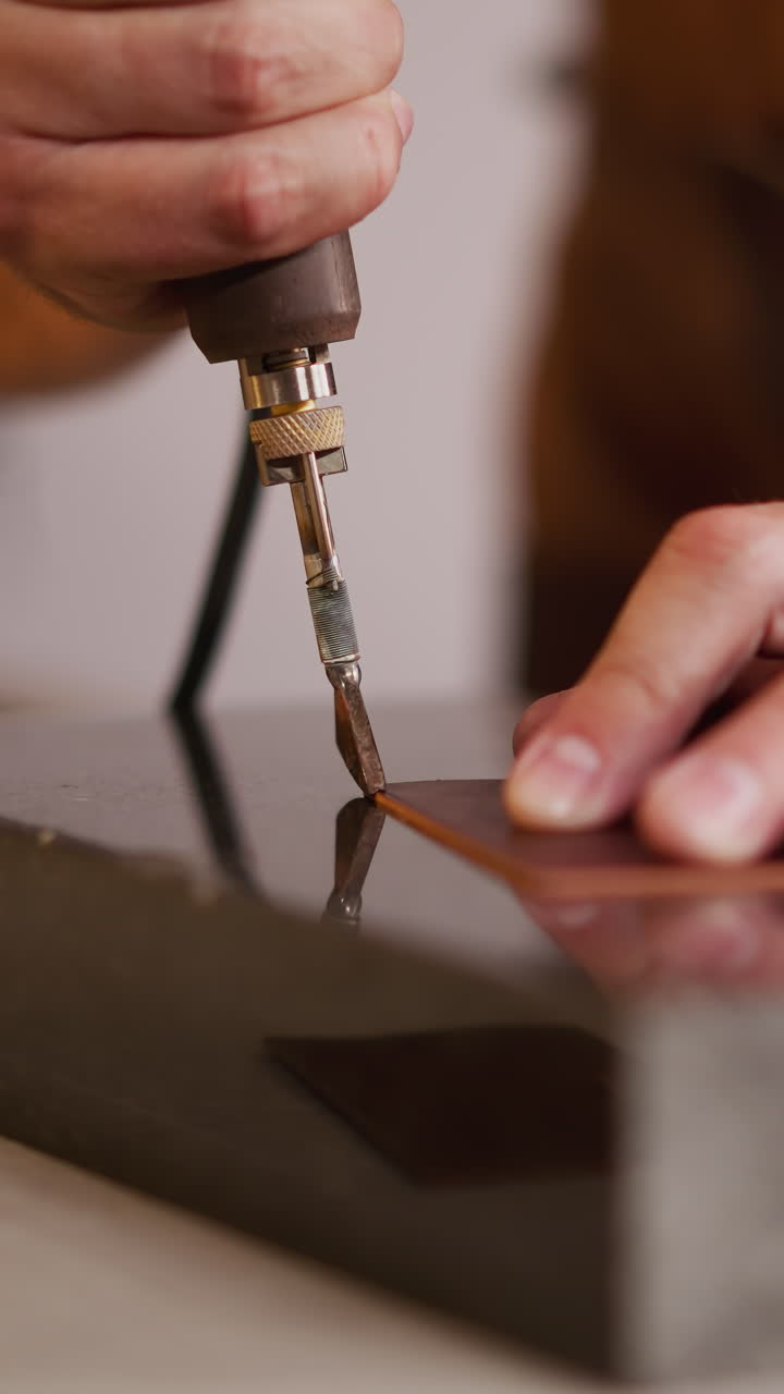 Master processes leather piece edge with special tool at workplace closeup. Craftsman makes item of traditional material in studio. Skilled handyman