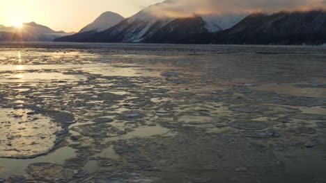 First-sunlight-shines-over-distant-mountain-range-in-Cook-Inlet,-aerial-tilt-up