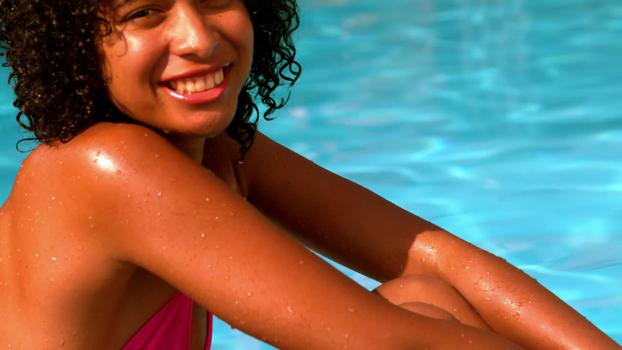 Donna felice in bikini rosa che sorride alla telecamera a bordo piscina