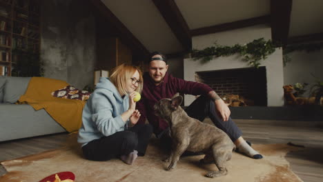 couple playing with her bulldog dog with a tennis ball on the floor in living room 2