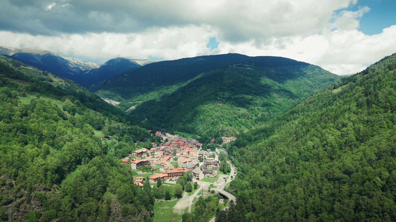 Drone orbit shot revealing Setcases mountain town surrounded by forest and valley landscape in Catalonia.