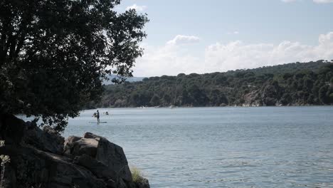 Hermoso-Paisaje-Lacustre-Con-Gente-Disfrutando-De-Deportes-Acuáticos,-Kayak-Y-Surf-De-Remo,-En-El-Embalse-Pantano-De-San-Juan,-Madrid