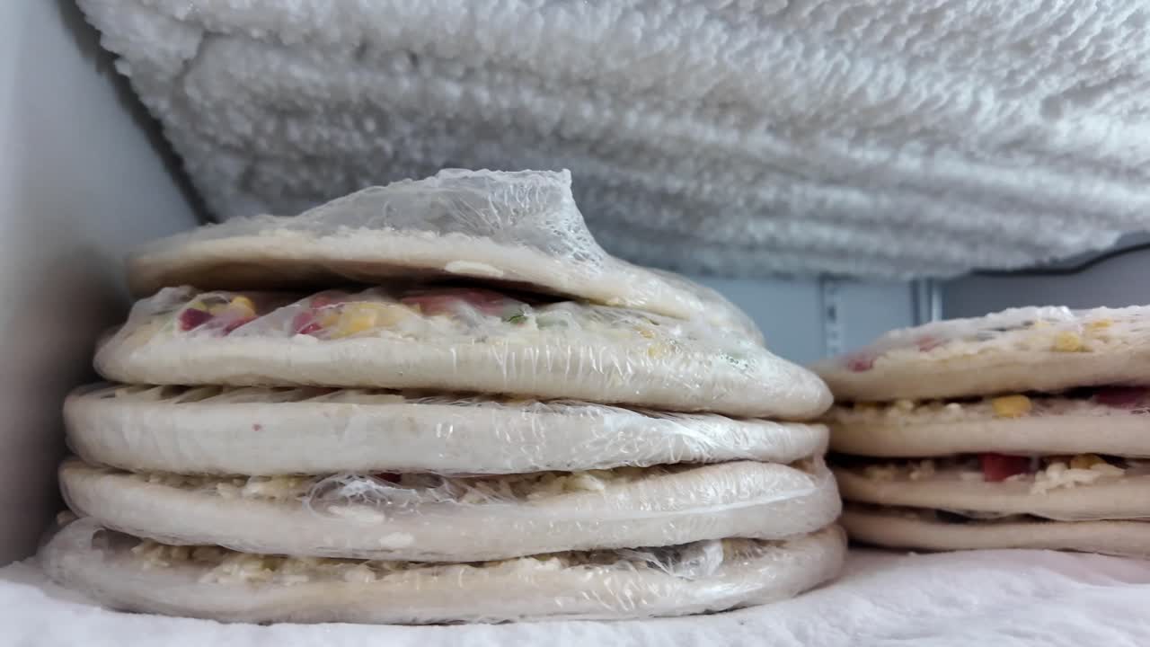 Stacks of frozen pizzas in a refrigerator