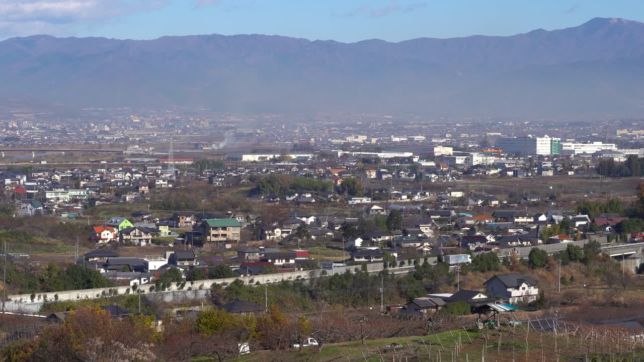 Beautiful Landscape Scenery Of Houses And Lush Trees In Yamanashi Prefecture In Japan With Vehicles Travelling On The Asphalt Road And Majestic Mountain In The Background - Wide Shot