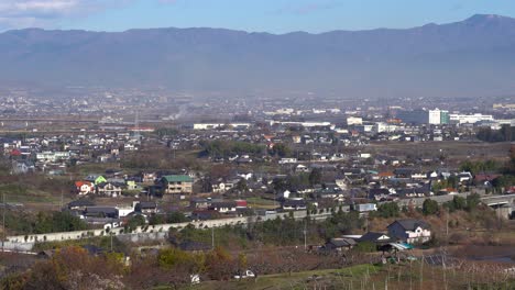 beautiful landscape scenery of houses and lush trees in yamanashi prefecture in japan with vehicles travelling on the asphalt road and majestic mountain in the background - wide shot
