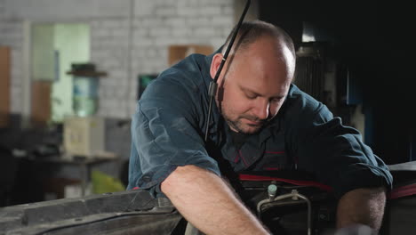 mechanic in blue uniform drops tool and collects another from colleague while working on car engine in automobile shop, focused auto repair professional performing hands-on maintenance