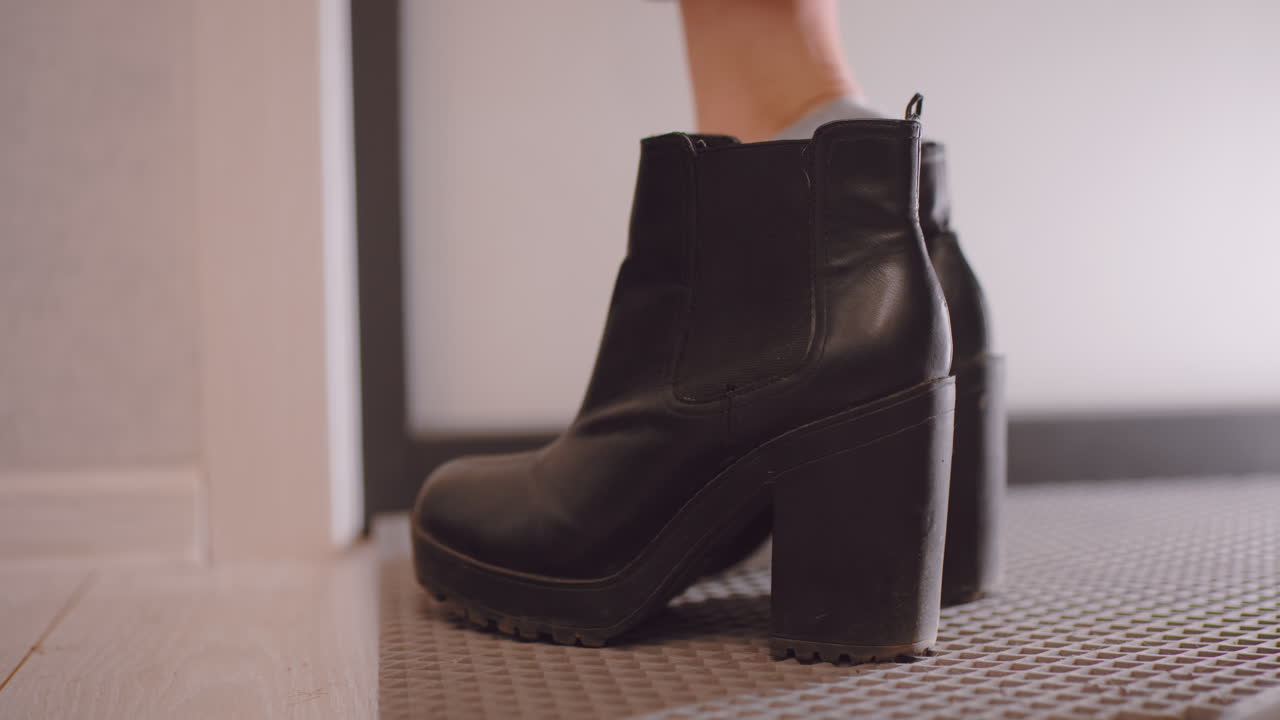 Close up of black leather high heel boot on floor as female puts on footwear at home entrance, showing stylish design, everyday routine, and detail of shoe preparation before leaving