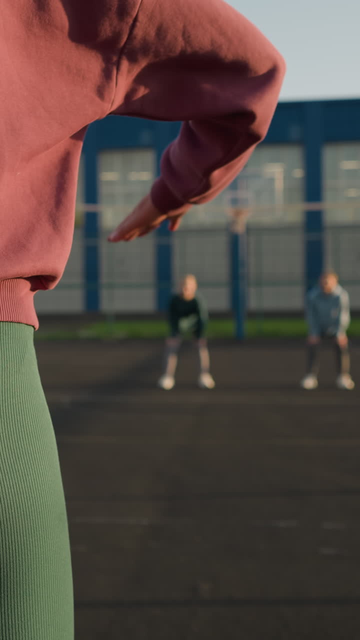 초록색 레을 입은 여성이 배경에 흐릿한 사람과 건물을 가지고 볼리볼을 뛰는 클로즈업, 역동적인 스포츠 환경에서 운동과 야외 활동을 보여줍니다.