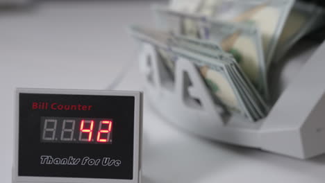 little black screen of commercial equipment with changing numbers. american dollars are counted at backdrop in blur.