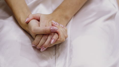 woman-holds-hands-with-pink-glitter-manicure-on-white-fabric