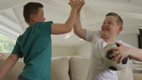 happy caucasian boy with brother watching tv and holding football in living room