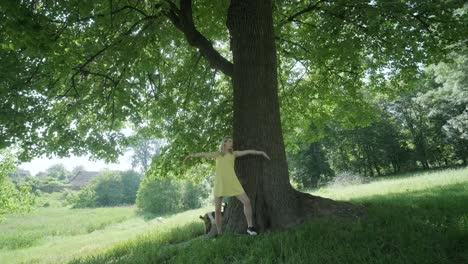 woman in yellow dress dancing by tree in summer park