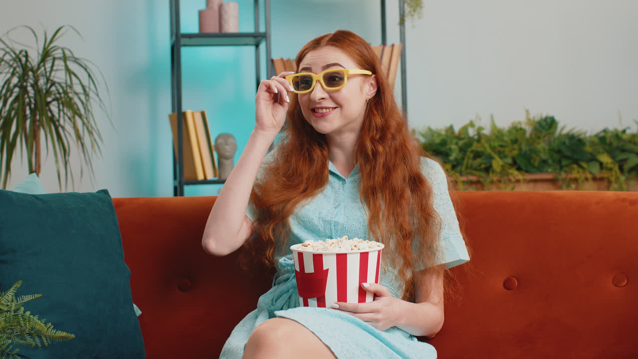 mujer sentada en el sofá comiendo palomitas de maíz y viendo interesantes películas de televisión en 3d, juegos deportivos en línea en casa