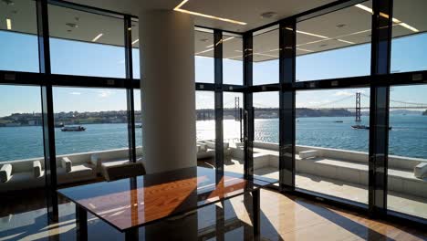 sunlight illuminates a modern office space, revealing a large wooden table and floor to ceiling windows offering breathtaking views of a bridge, boats, and a cityscape across a wide body of water
