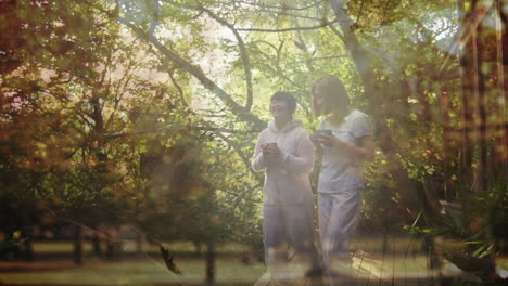 animation of happy asian mother and daughter walking and drinking tea over leaves falling