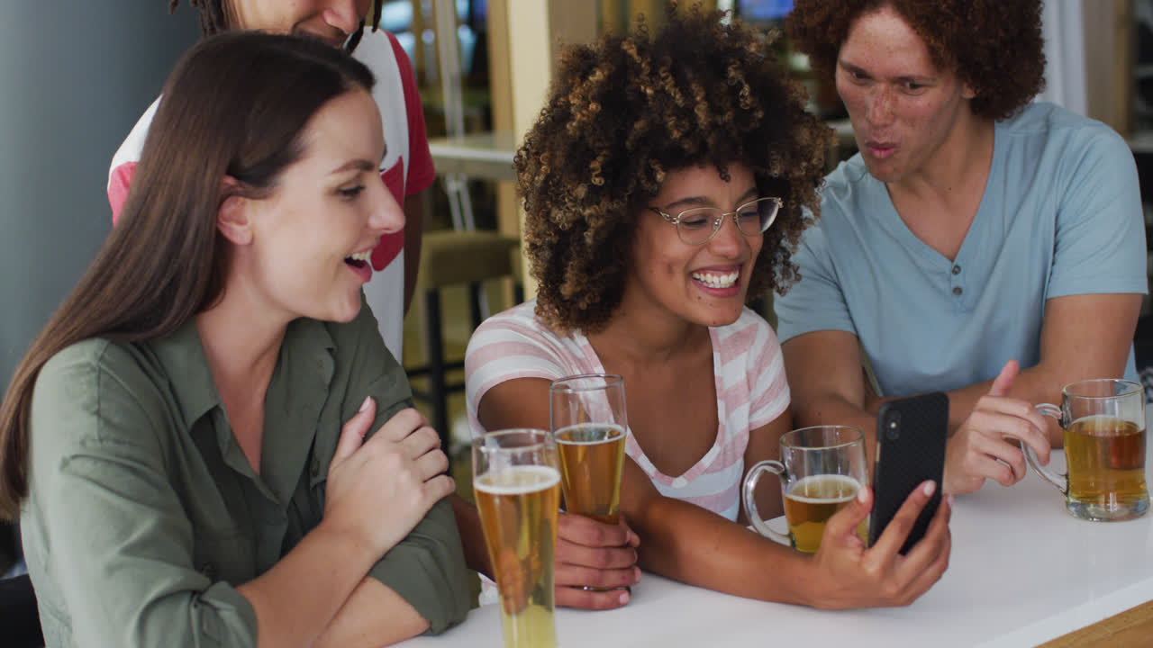 un grupo diverso de amigos felices bebiendo cervezas y usando un teléfono inteligente en un bar