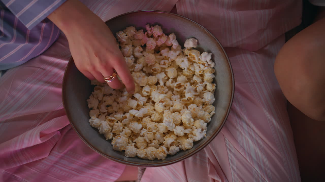 Friends fingers grabbing popcorn from bowl at home pajamas party closeup