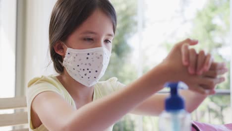 girl wearing face mask sanitizing her hands at home