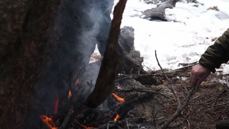 unseen man builds campfire against boulder in cold winter camp scene