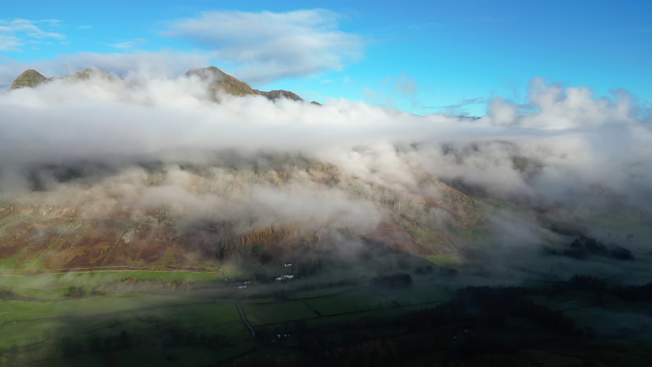 초록색 그림자 계곡과 구름으로 뒤인 산은 이른 아침 가을의 빛에 비추어져 있습니다.