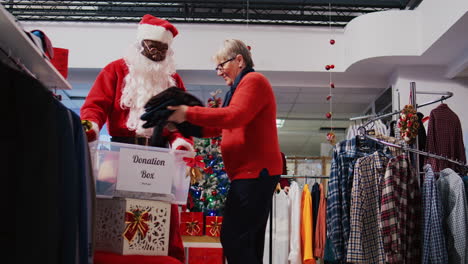 staff assistant wearing santa claus costume in clothing store collecting clothes from altruist clients in donation container, giving them as present during xmas season charity efforts