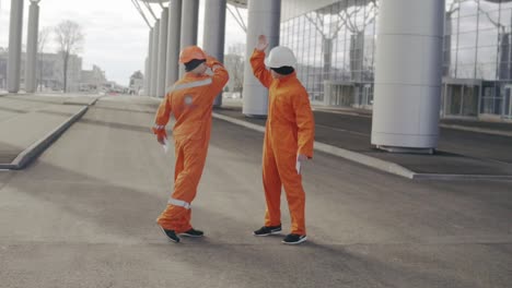 Two-construction-workers-in-orange-uniform-giving-high-five.-They-look-very-happy.-New-constructed-building-with-columns-at-the