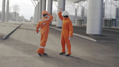 two construction workers in orange uniform giving high five. they look very happy. new constructed building with columns at the