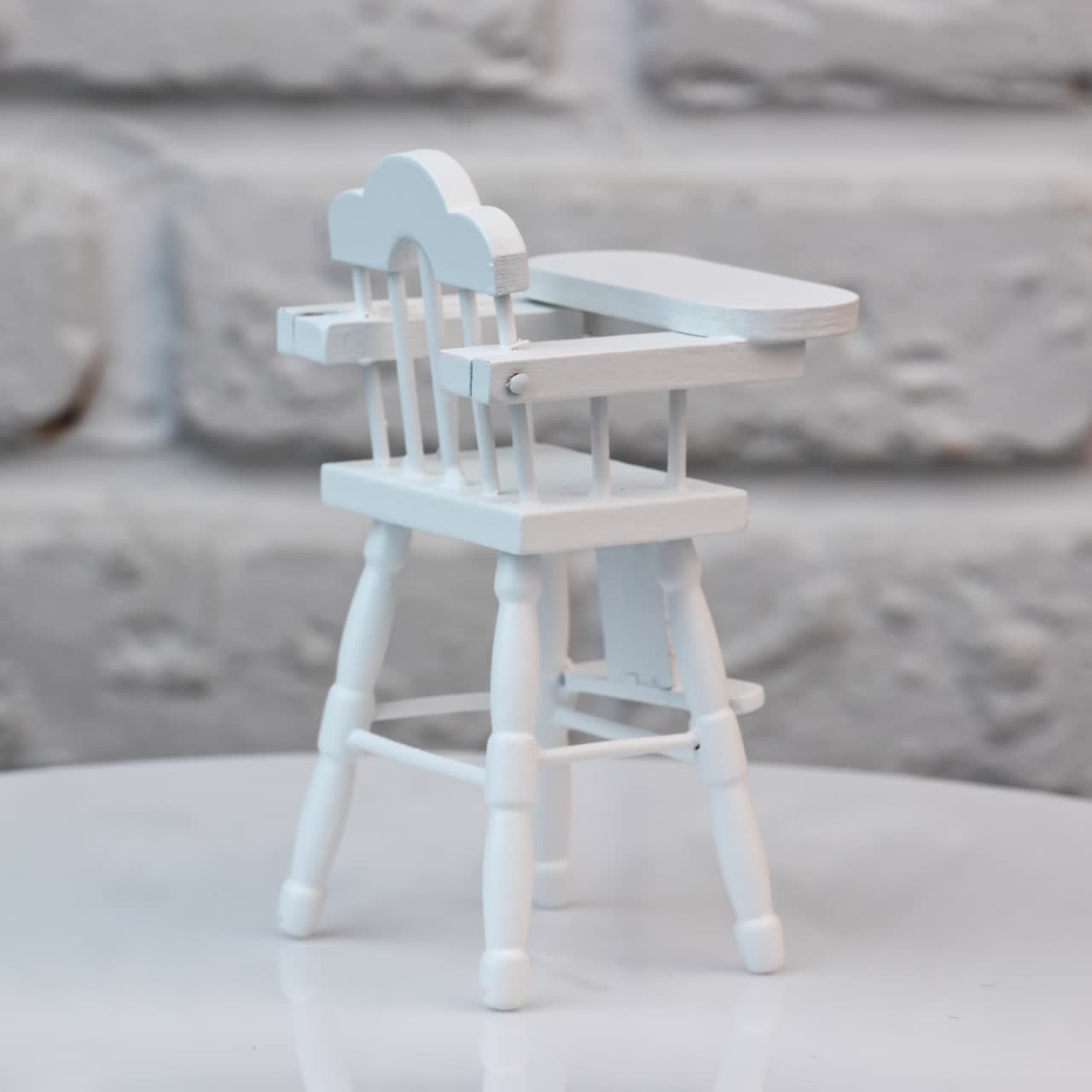 Baby feeding chair painted white at the rotating table. Carved wooden furniture item for kid's play. Close up