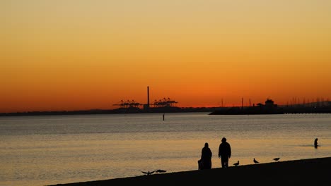 couple walking along beach during sunset