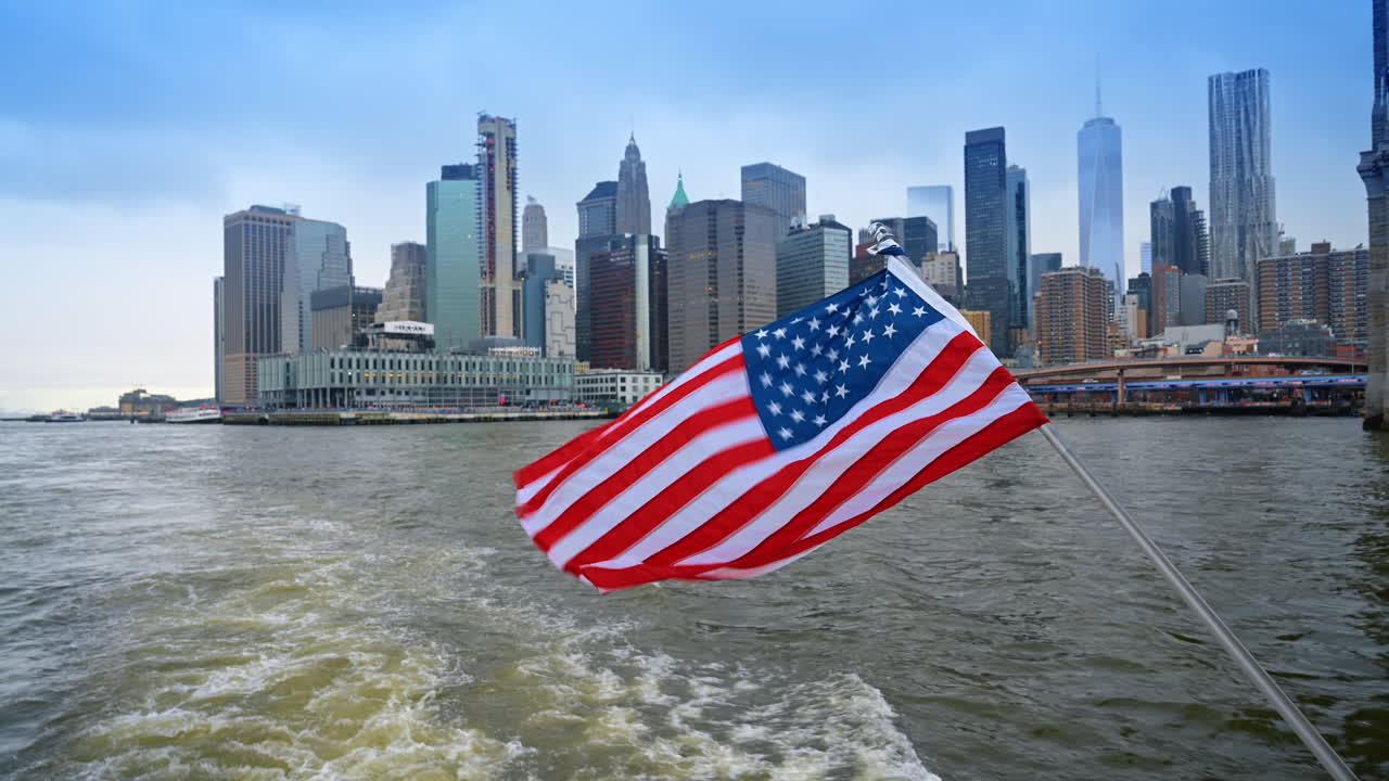 Skyline di Lower Manhattan con il One World Trade Center e la bandiera. Bandiera degli Stati Uniti su una barca che si muove attraverso il porto con i grattacieli di Lower Manhattan sullo sfondo