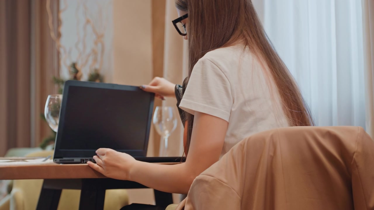 Giovane donna che disimballa il laptop al tavolo, preparando la postazione di lavoro remota con movimenti attenti; i ruoli di freelance e studentessa si alternano tra sistemare il caricabatterie, posizionare lo schermo e concentrarsi.