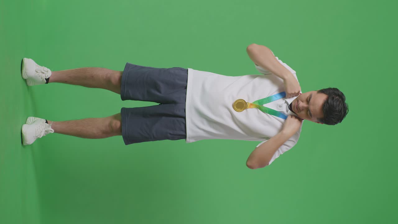 Full Body Of Asian Man Wearing A Gold Medal And Smiling To Camera Being Proud Winning As The First Winner On Green Screen Background In The Studio